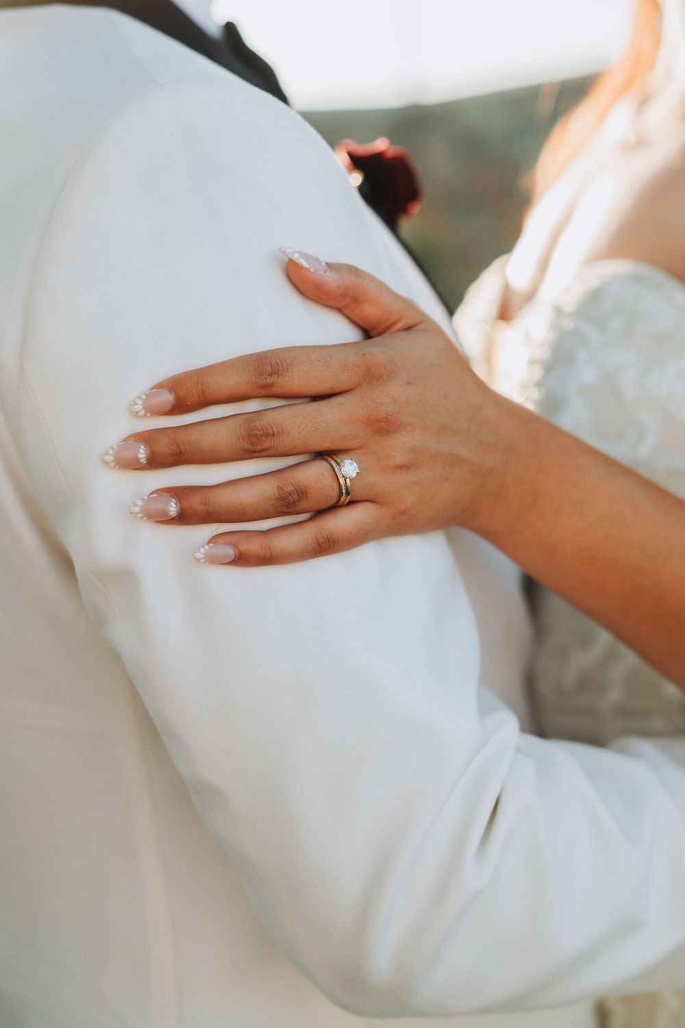 A hand wearing a diamond wedding ring rests delicately on a white fabric surface, creating an elegant bridal detail.