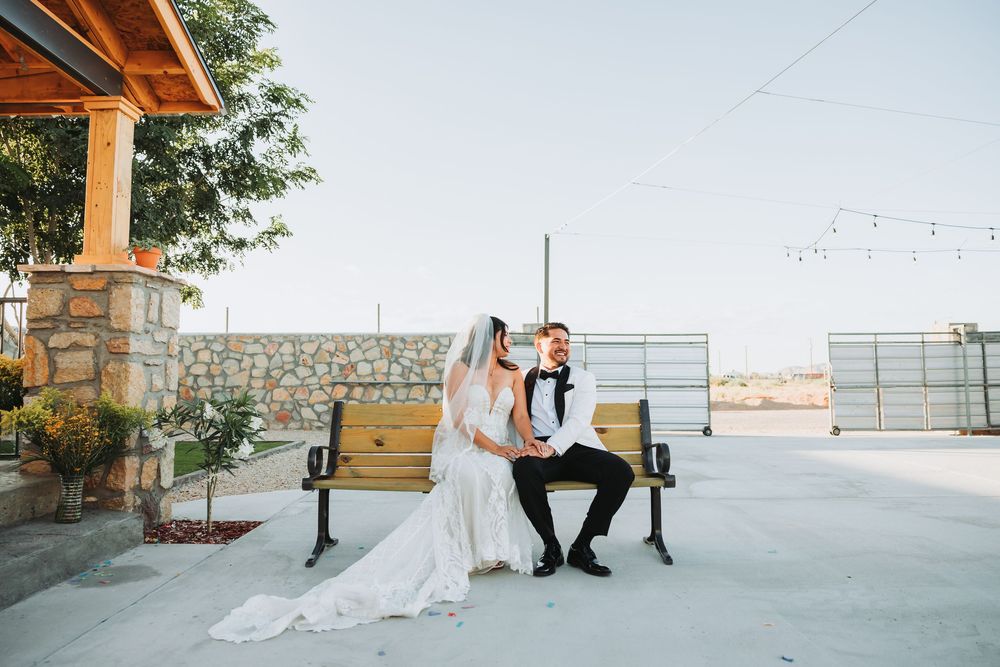 A couple shares a romantic moment on a rustic wooden bench with mountain views and stone pillars in the background.