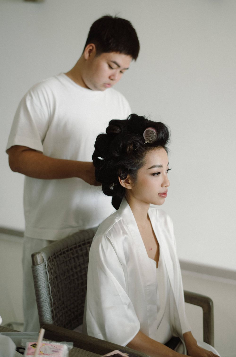 A person in a white robe sits at a dressing table while getting ready for a formal event.