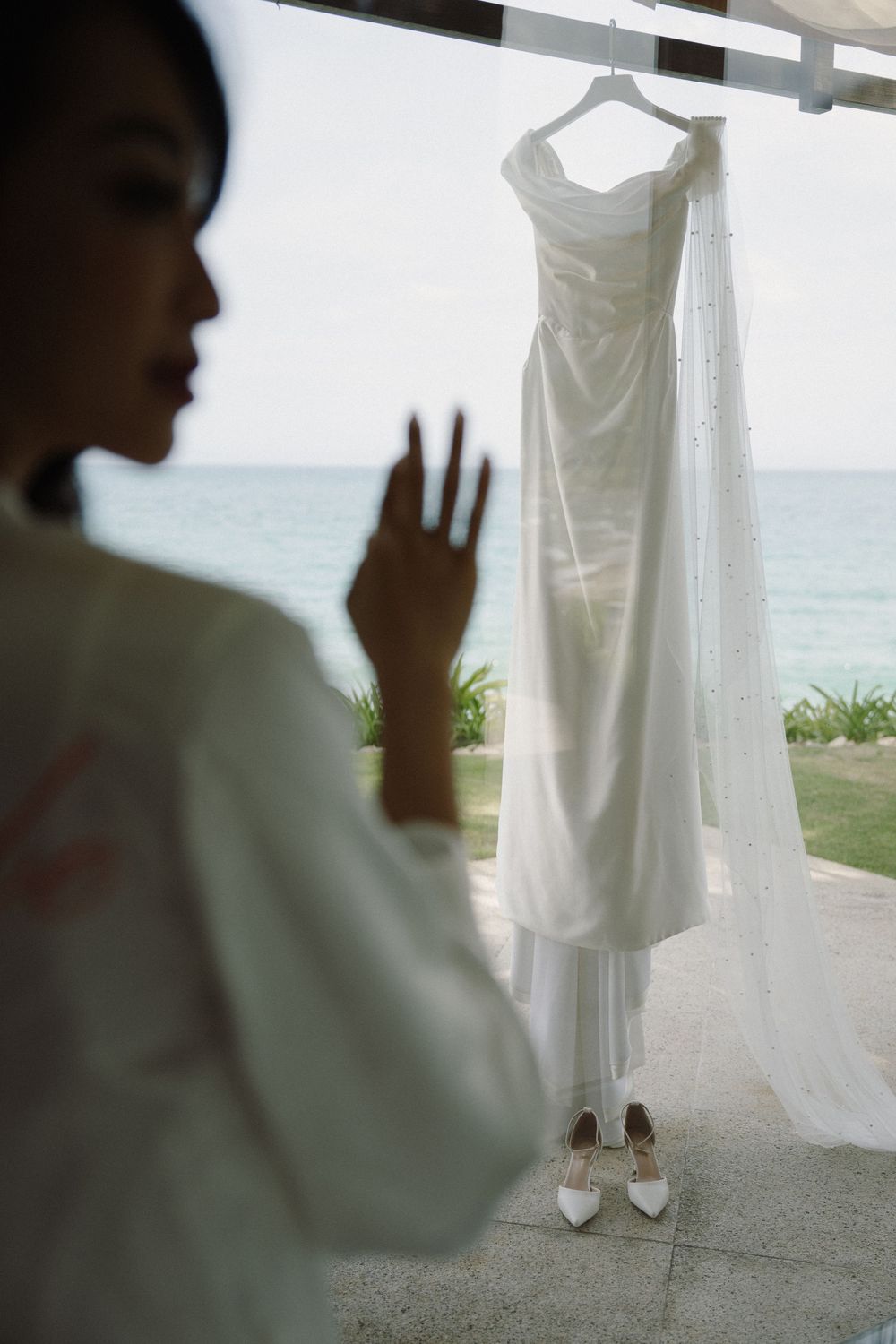 White wedding dress hanging by oceanside vista with elegant shoes beneath.