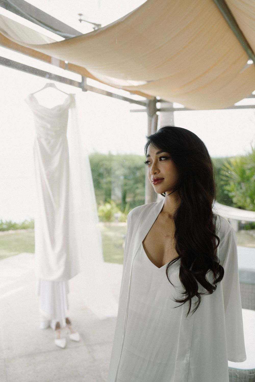Woman in a flowing white dress poses gracefully outdoors under a canopy.