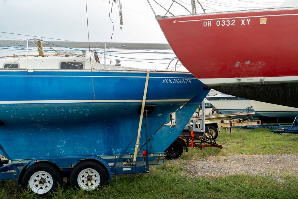 A series of boat hulls and trailers lined up in a marina storage yard show various sizes and colors of vessels.