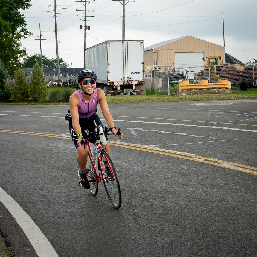 A cyclist in bright athletic wear leans forward while riding a road bike on an empty asphalt street.