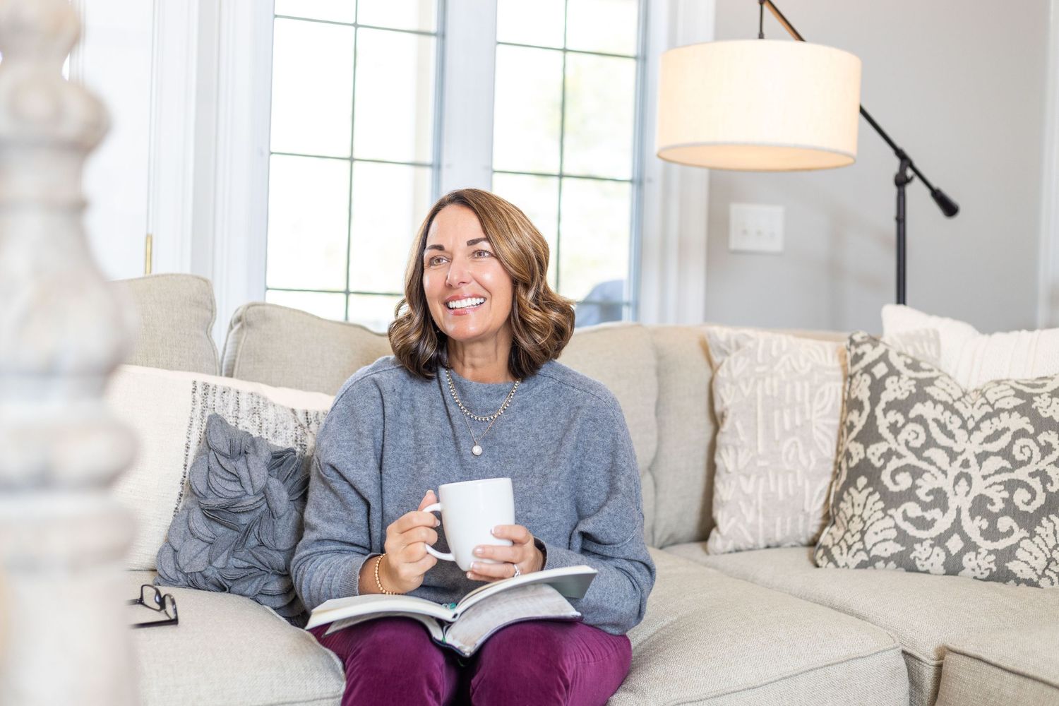 Cozy home interior with person reading on white couch surrounded by decorative pillows.