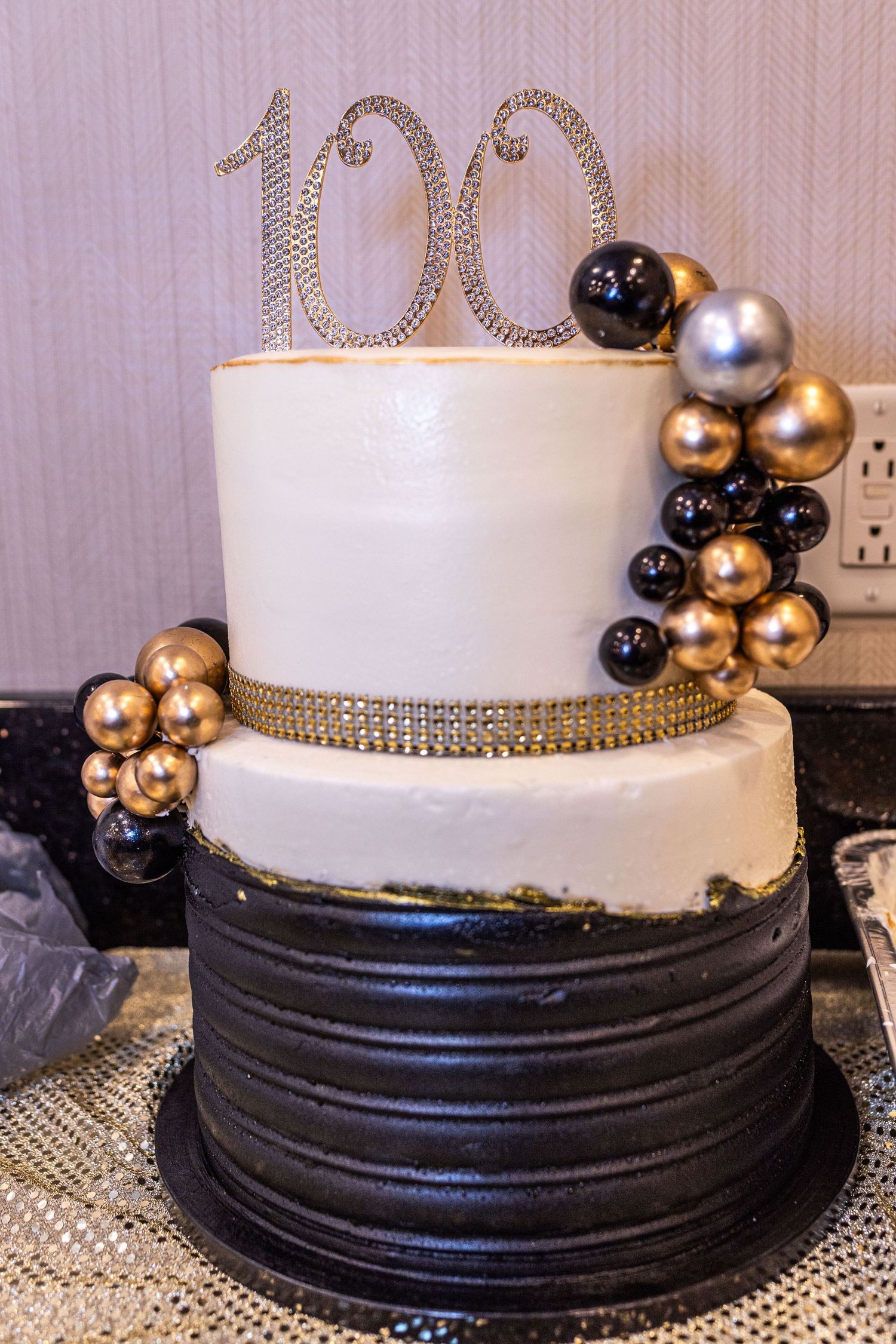 Elegant white wedding cake decorated with black base trim and metallic gold and silver balloon accents.