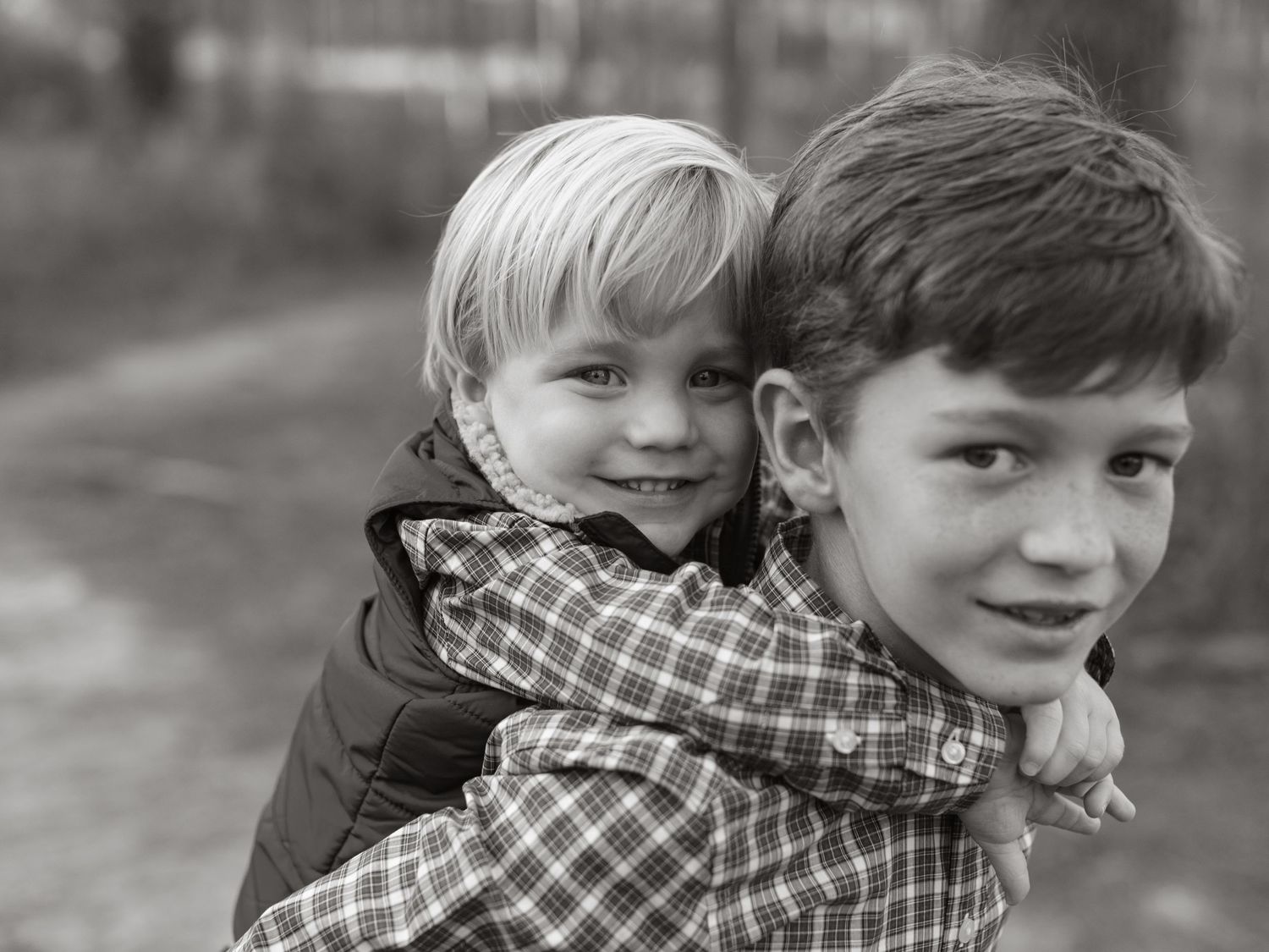 Black and white portrait of two young children with one giving a piggyback ride to the other outdoors.