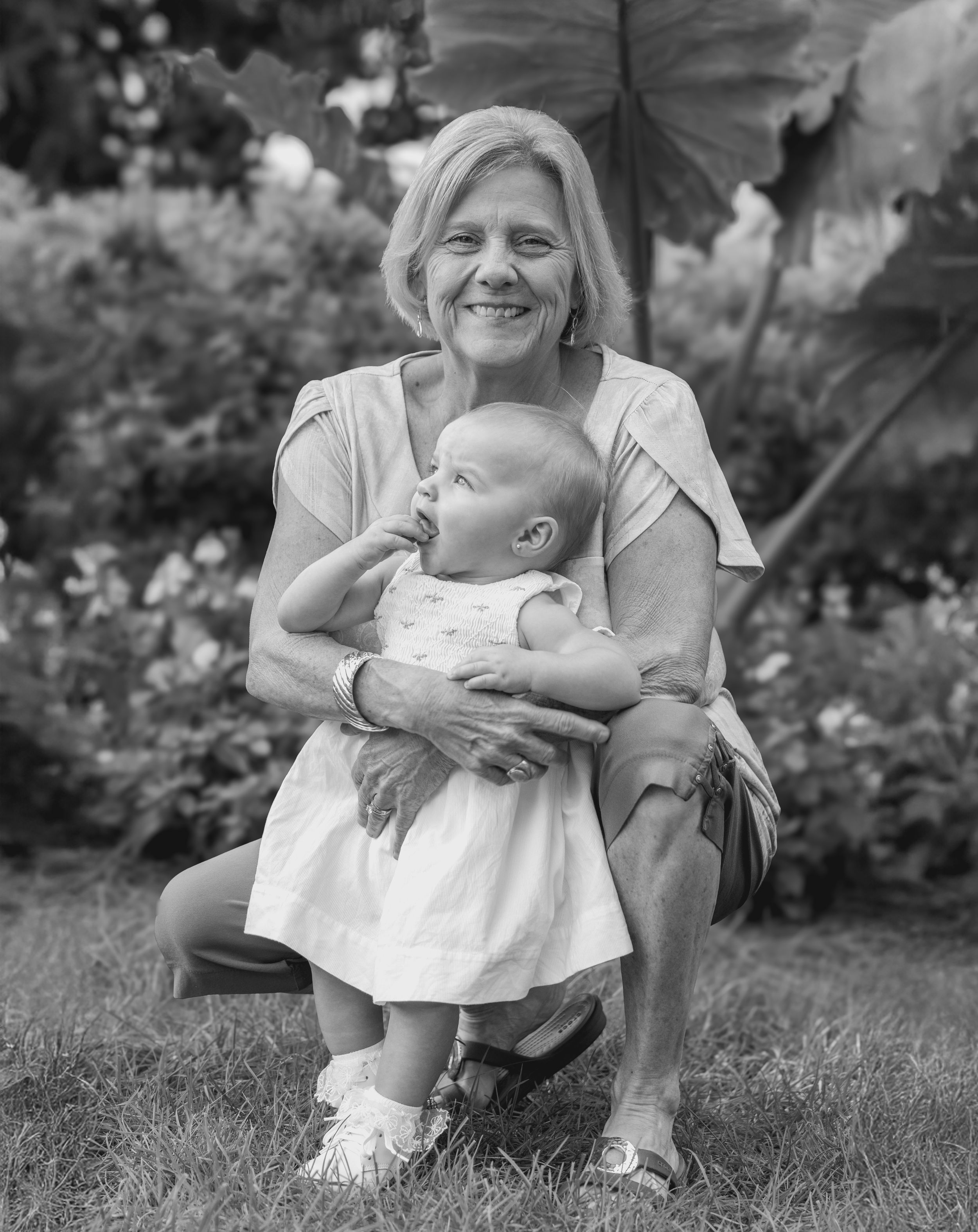 A heartwarming black and white portrait of a caregiver holding a baby in a garden.