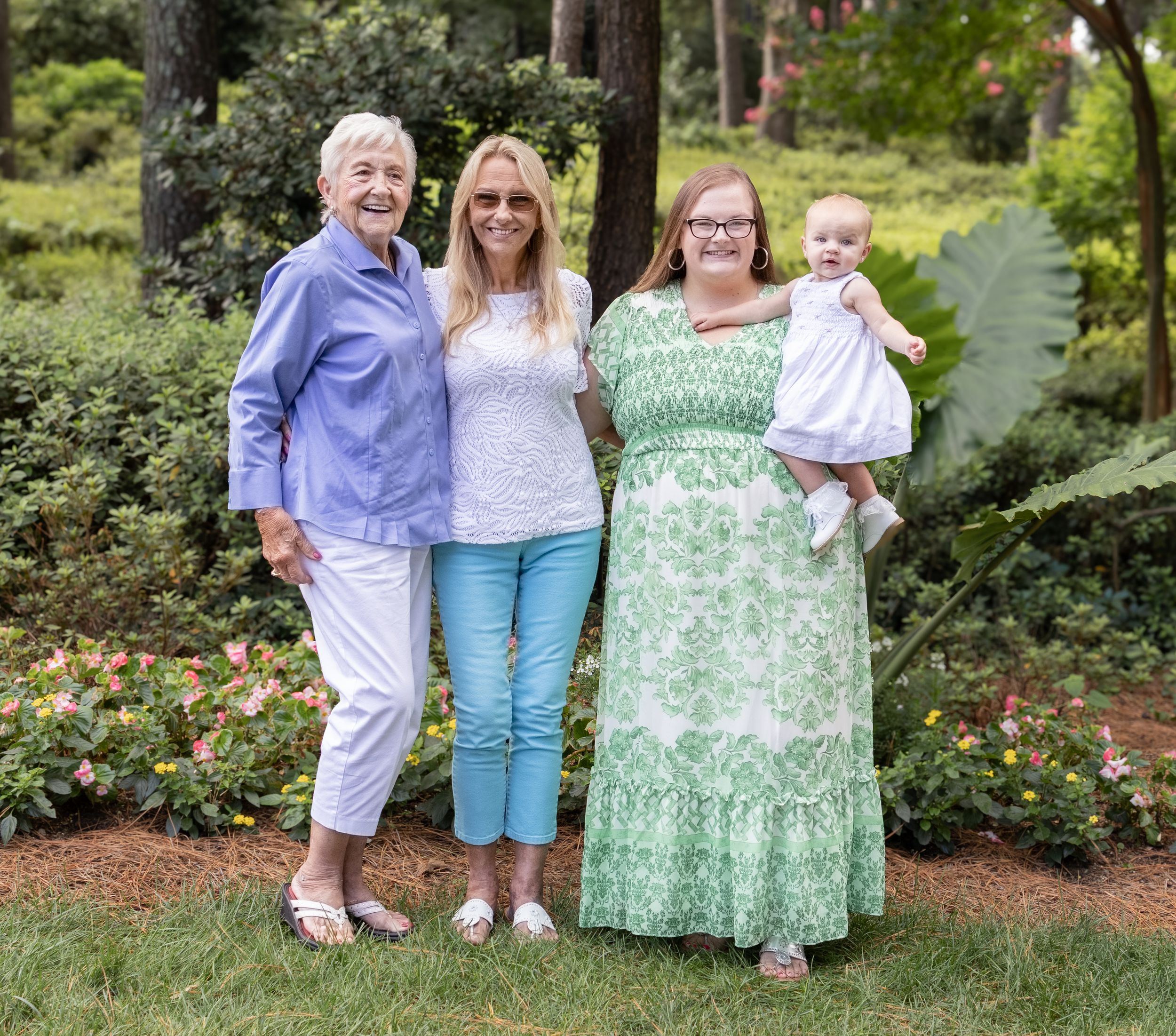 Four generations of family members pose together in a lush garden setting.