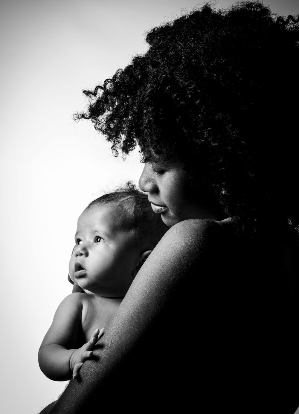 Schwarz-weiß Foto: Mama hält ihr Baby eng am Körper, beide mit freien Schultern. Zärtlicher, emotionaler Moment.