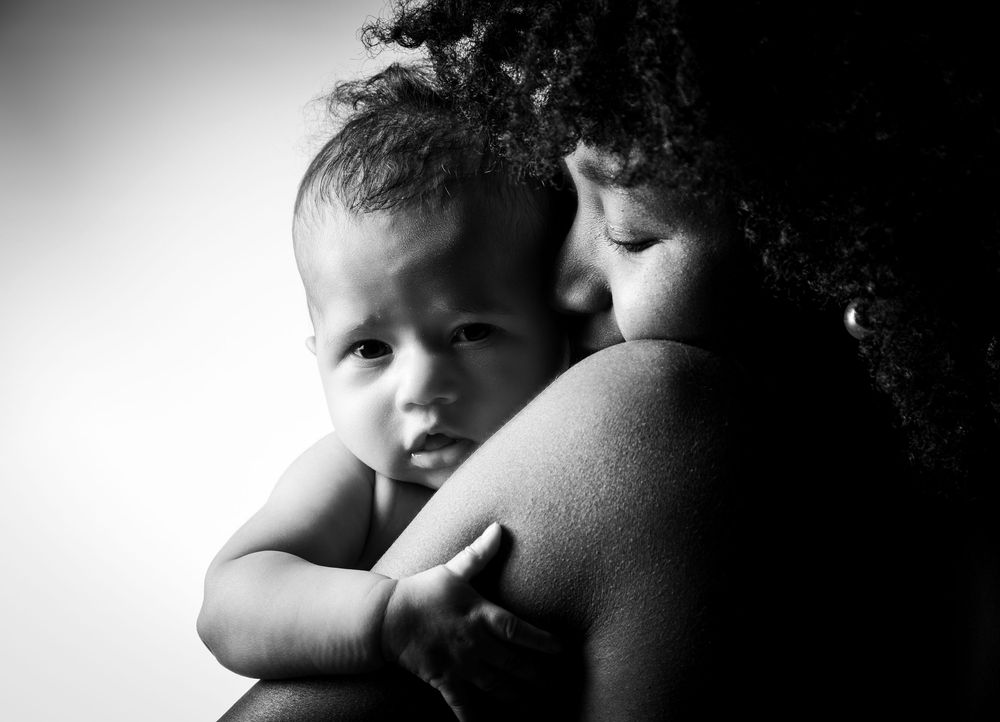 Ein kuschliges Foto von einer Mutter mit Baby in schwarz/weiß.Von beiden sieht man die nackten Schultern. Ein intimer Moment im Fotostudio.