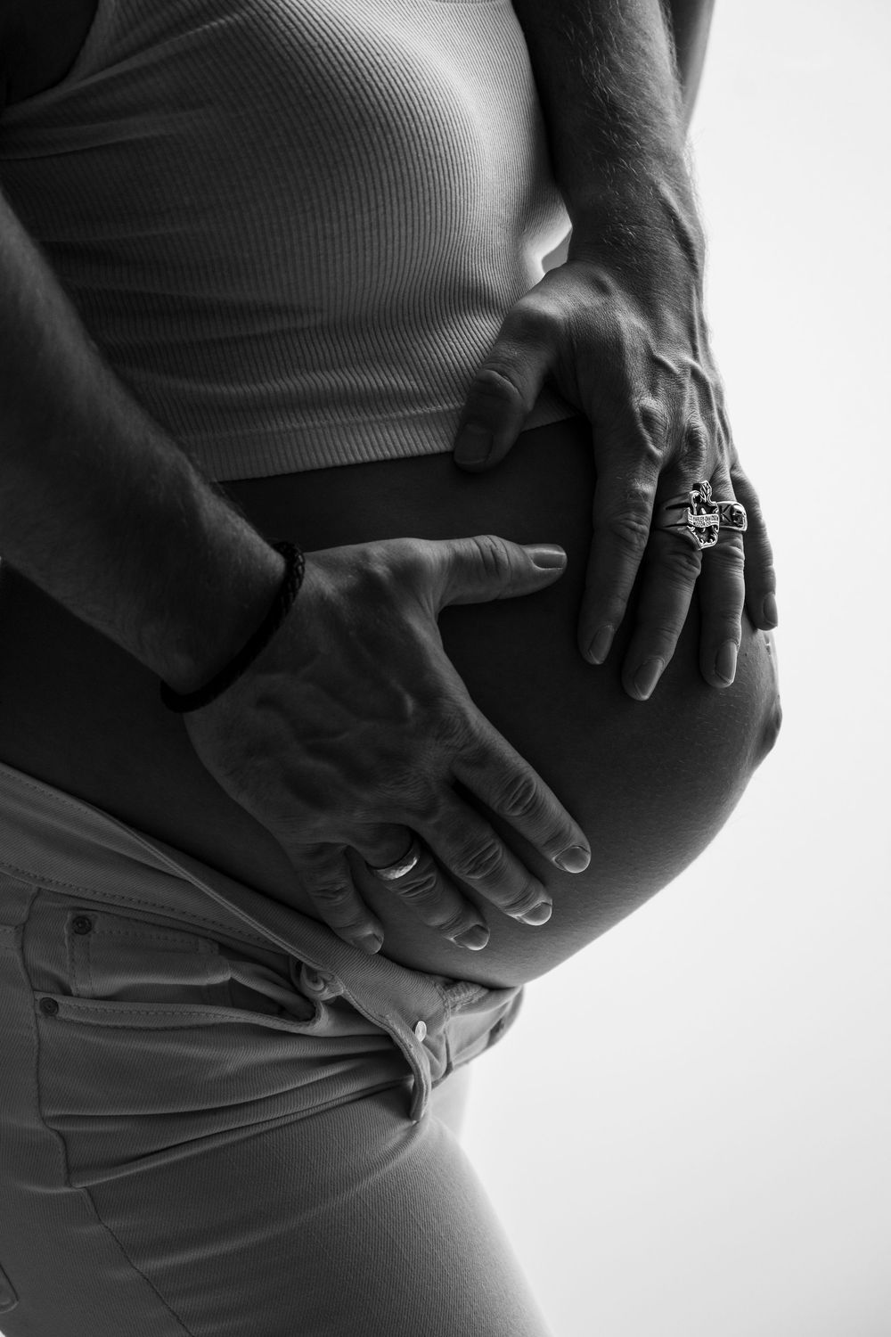 Ein close up Foto in schwarz/ weiß, von einem Babybauch. Es liegen die Hände des werdenden Vaters auf dem Bauch.