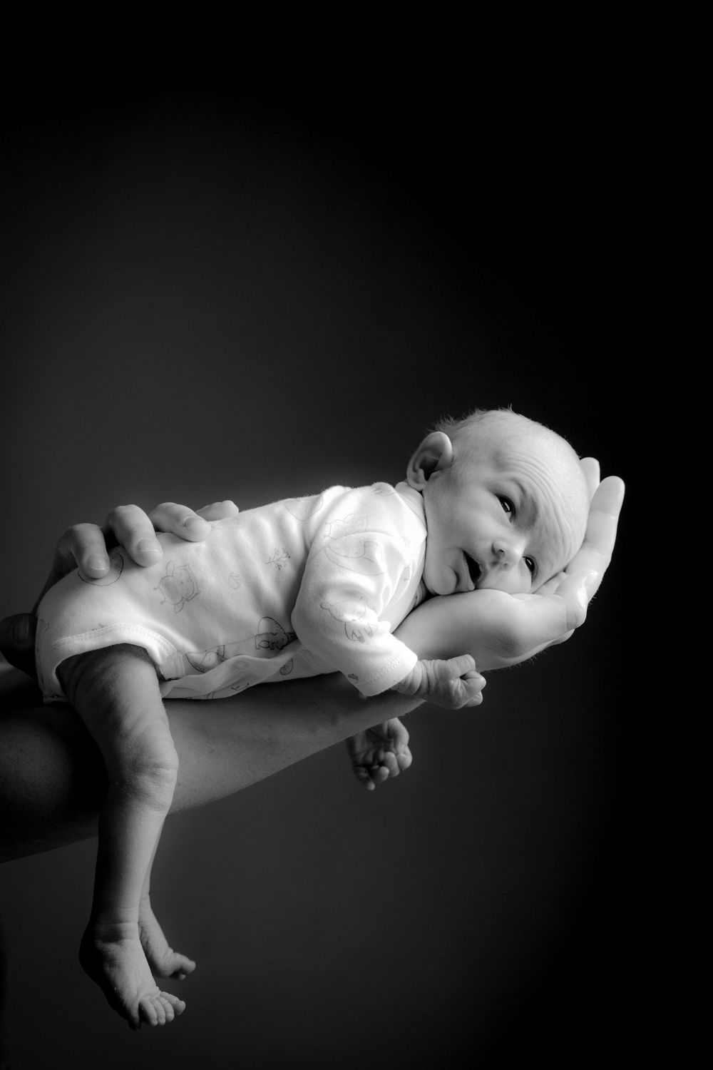Ein schwarz/weiß Foto eines Babys ,dass auf dem ausgestreckten Arm des Vaters liegt. Es schläft und fühlt sich wohl. Studiofotogafie Hassel