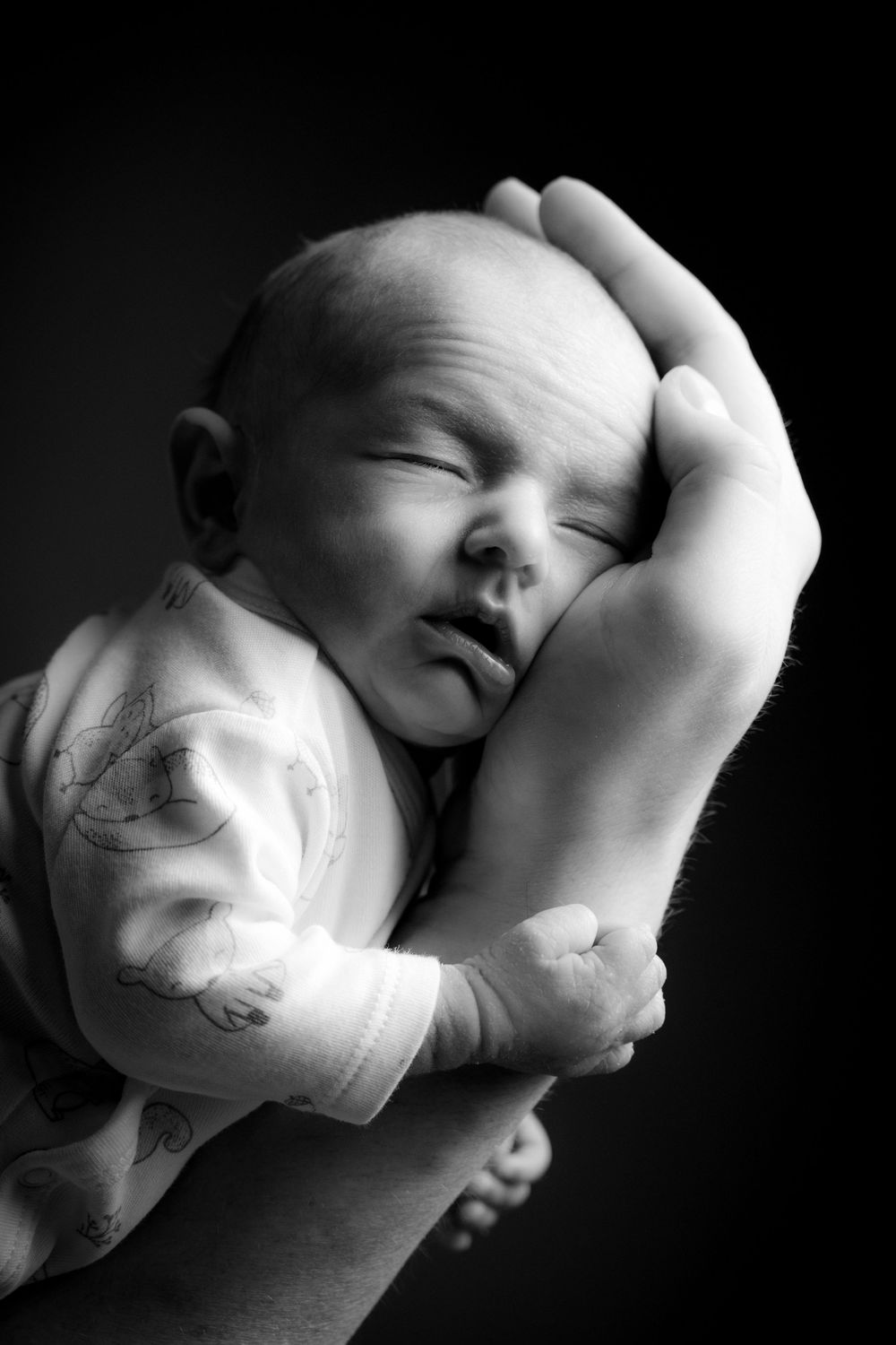 Ein schwarz/weiß Foto vom Gesicht eines Babys dass auf der Hand des Vaters liegt.  Es ist ein Studiofoto , fotografiert in Gelsenkirchen.