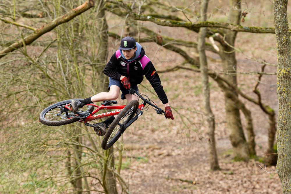 Mountain biker performs a series of dynamic jumps and tricks through a wooded trail course.