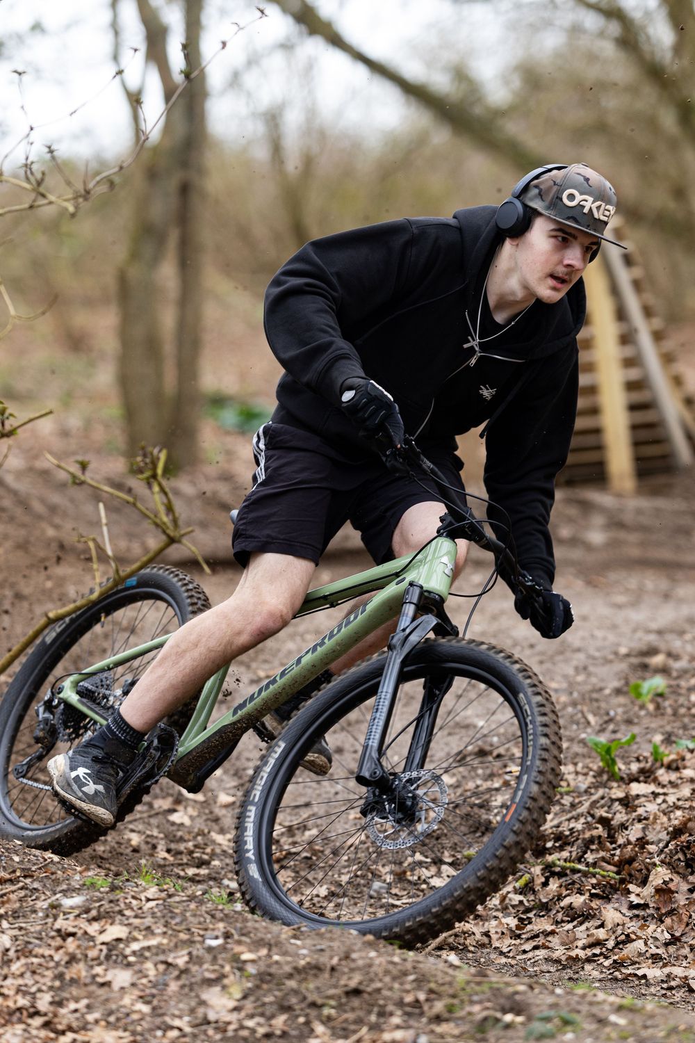 Mountain biker leans into a sharp turn on a dirt trail through autumn woods, demonstrating advanced cornering technique.