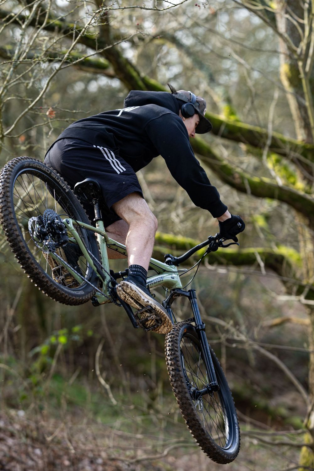 Mountain biker performs impressive aerial tricks on a dirt jump trail through mossy forest terrain.