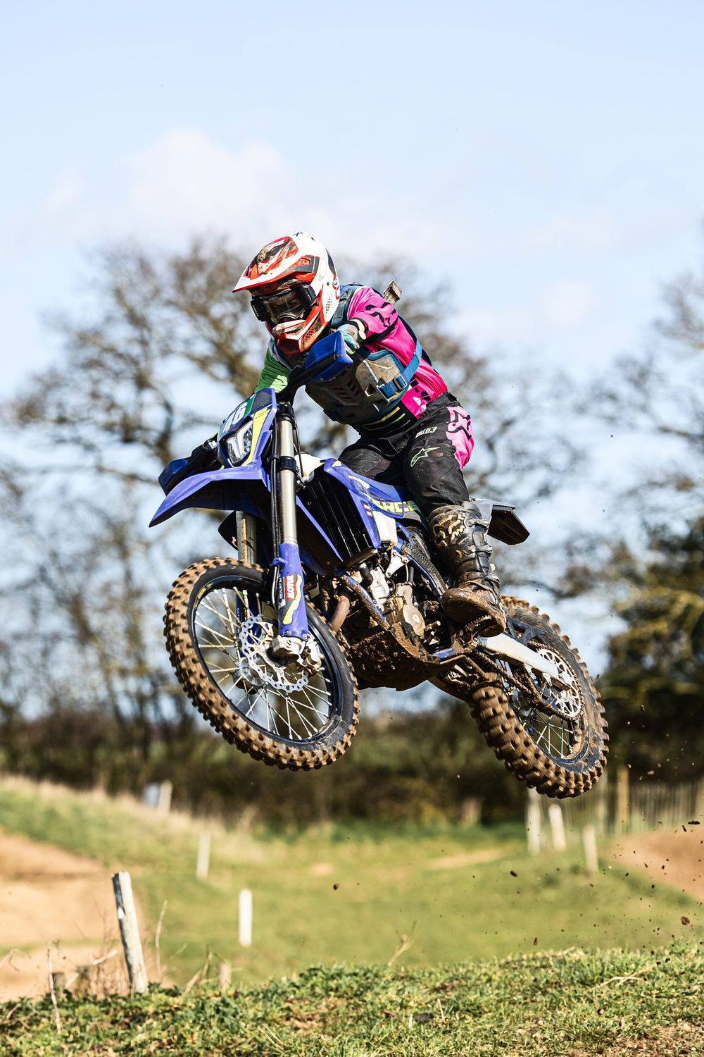 Dirt bike rider soaring through the air during a motocross jump on a grassy outdoor track.