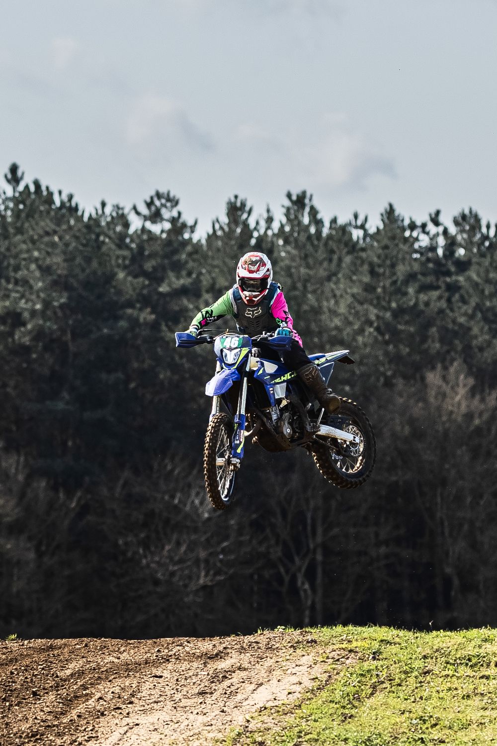 Dirt bike rider performs impressive aerial jump sequence over motocross track with pine forest backdrop.