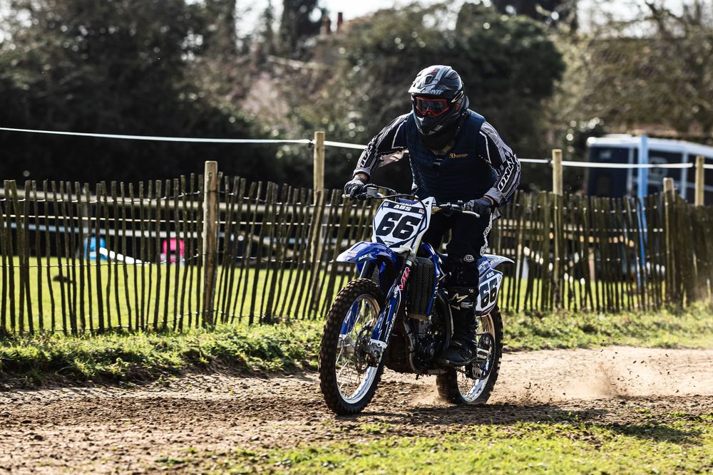 A motorcyclist navigates a dirt track turn during an off-road racing event on a sunny day.