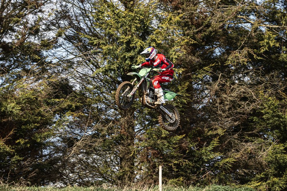Sequence of motocross action shots showing a rider performing jumps on a dirt bike against a wooded background.