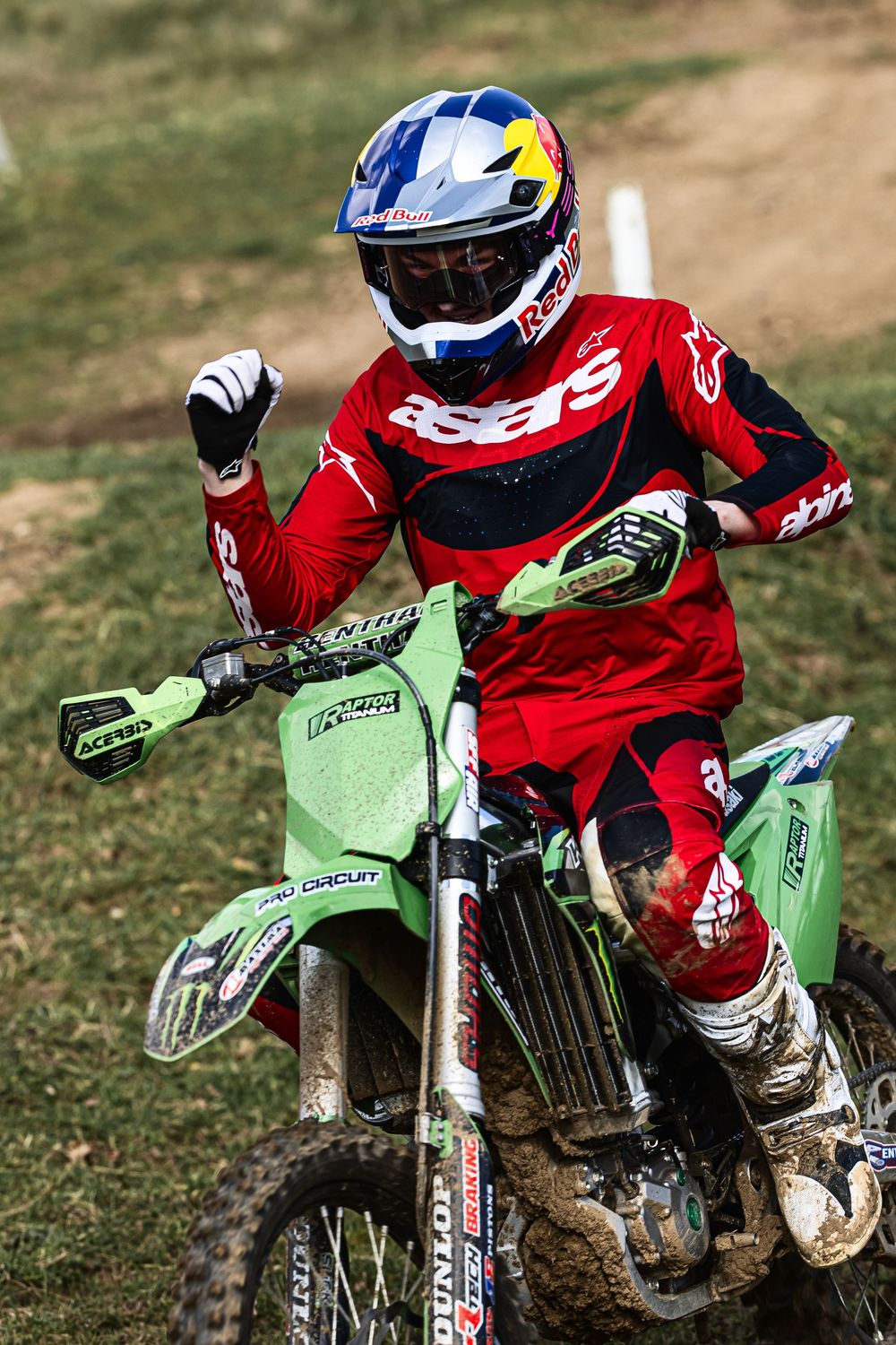 Multiple dirt bike riders in red gear racing on green Kawasaki motorcycles across a grassy terrain.