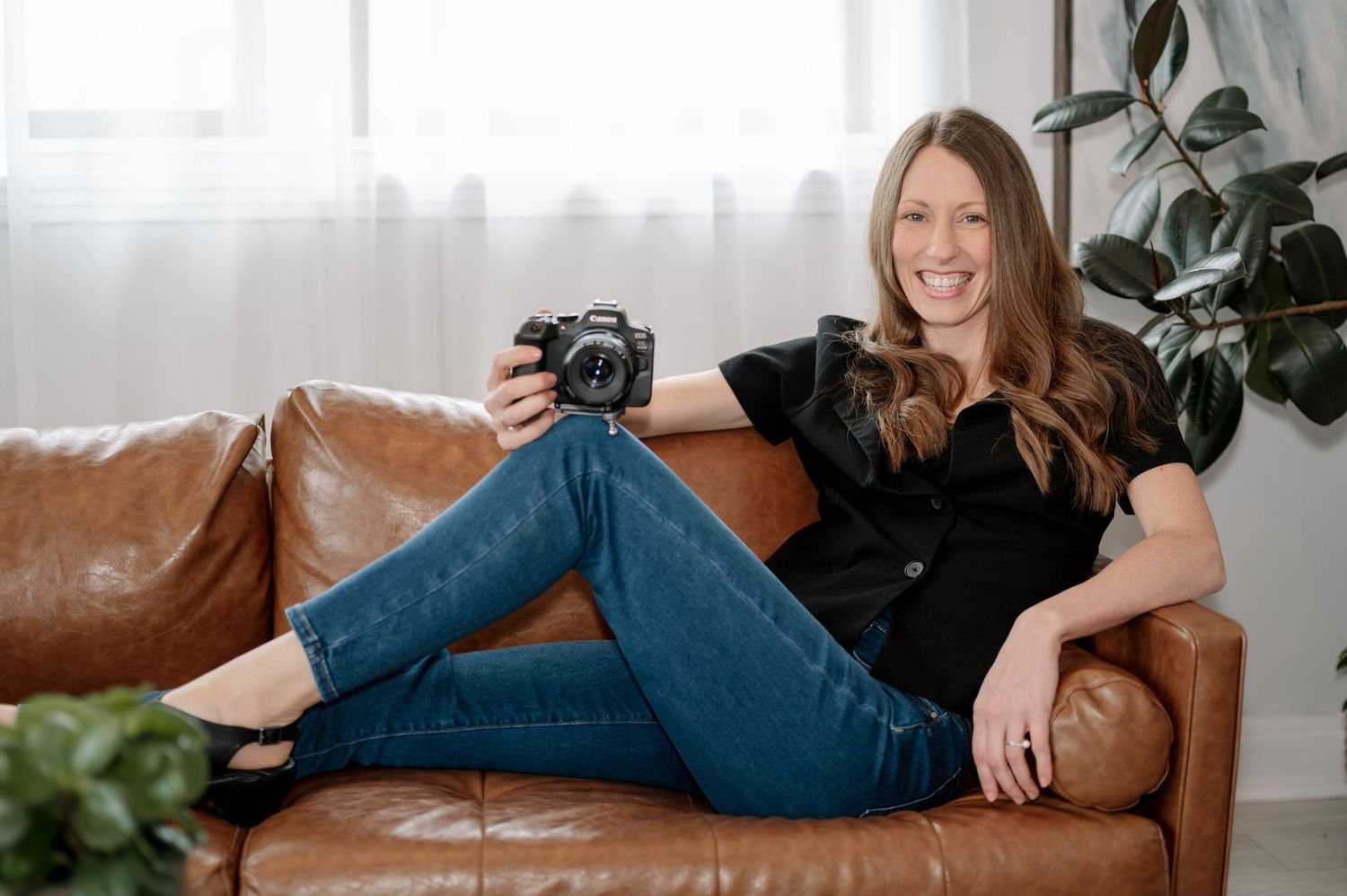 A photographer relaxes on a brown leather couch with a camera.