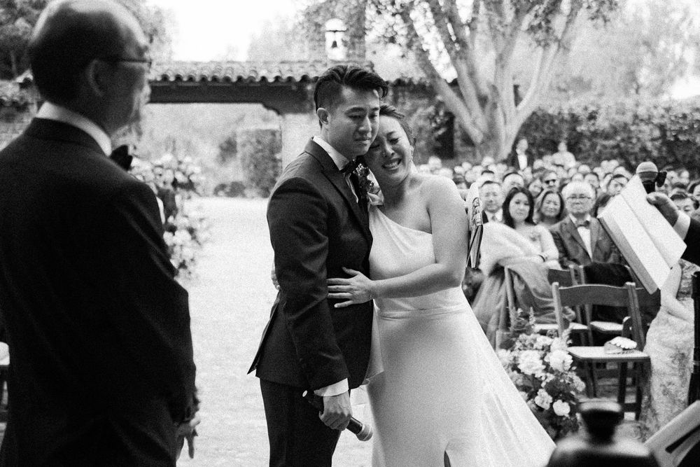 Emotional black and white photo of bride and groom embracing during outdoor wedding ceremony.
