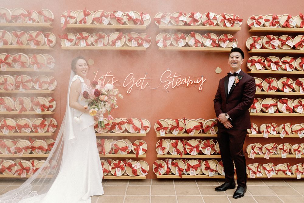 Couple poses in front of decorative pink wall display with neon sign at wedding reception.
