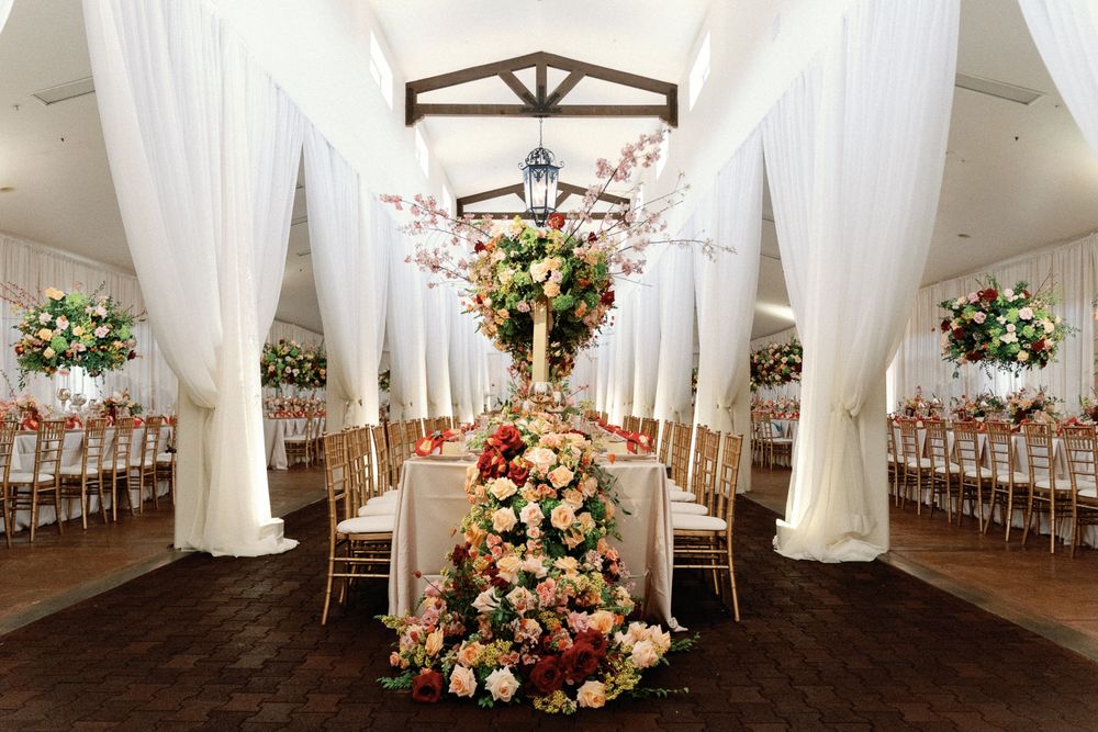 Elegant wedding reception hall with white draping, tall floral centerpieces, and candlelit tables.