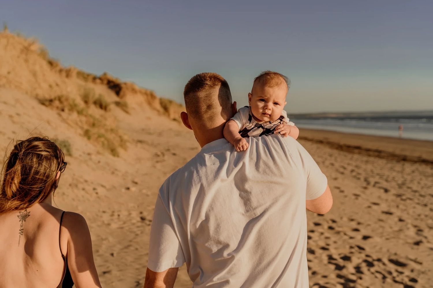 Candid family portraits on a sandy beach at sunset with golden light illuminating the coastal dunes.