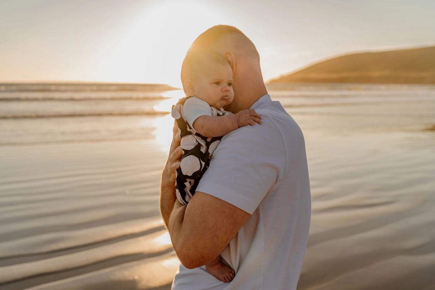 Couple shares romantic embrace on sunset beach with golden light reflecting off calm ocean waters.