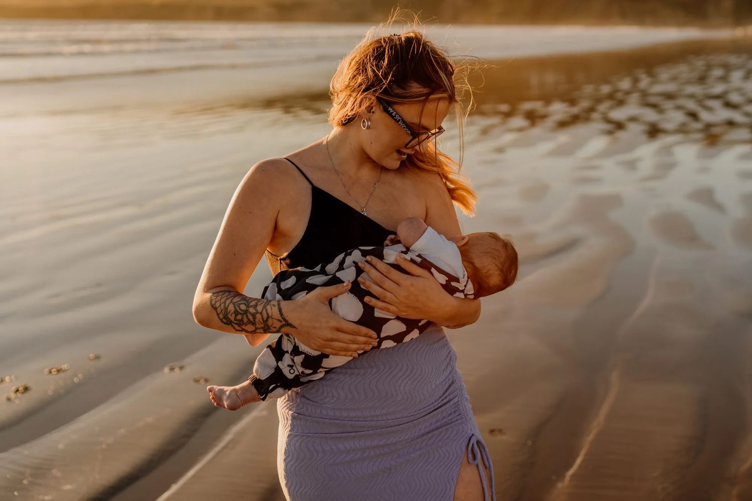 A family enjoys a tender beach moment at sunset with waves washing over bare feet in the sand.