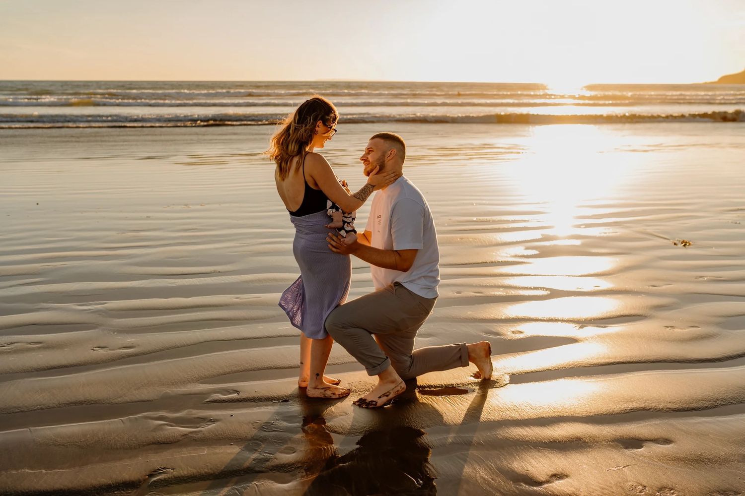 A romantic beach proposal scene with the sun setting over the ocean in the background.