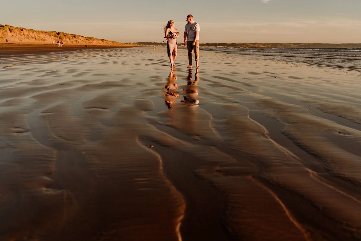Two silhouettes walk along wet sand patterns during golden hour on an empty beach.