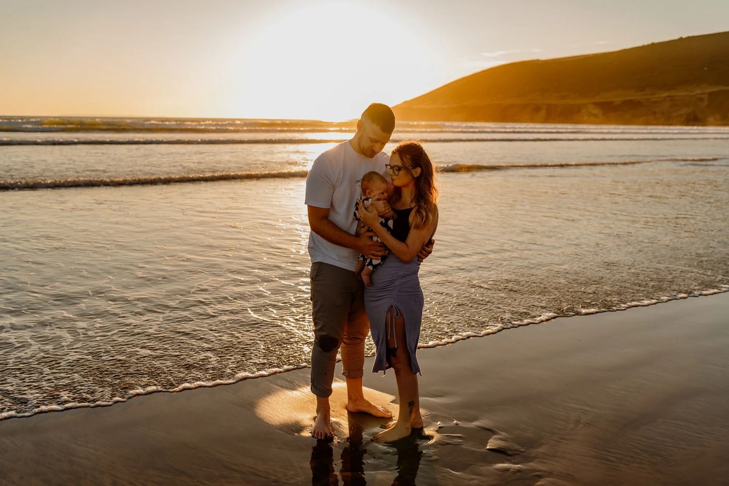 A couple walking hand in hand along a serene beach shoreline at golden sunset with reflective wet sand.