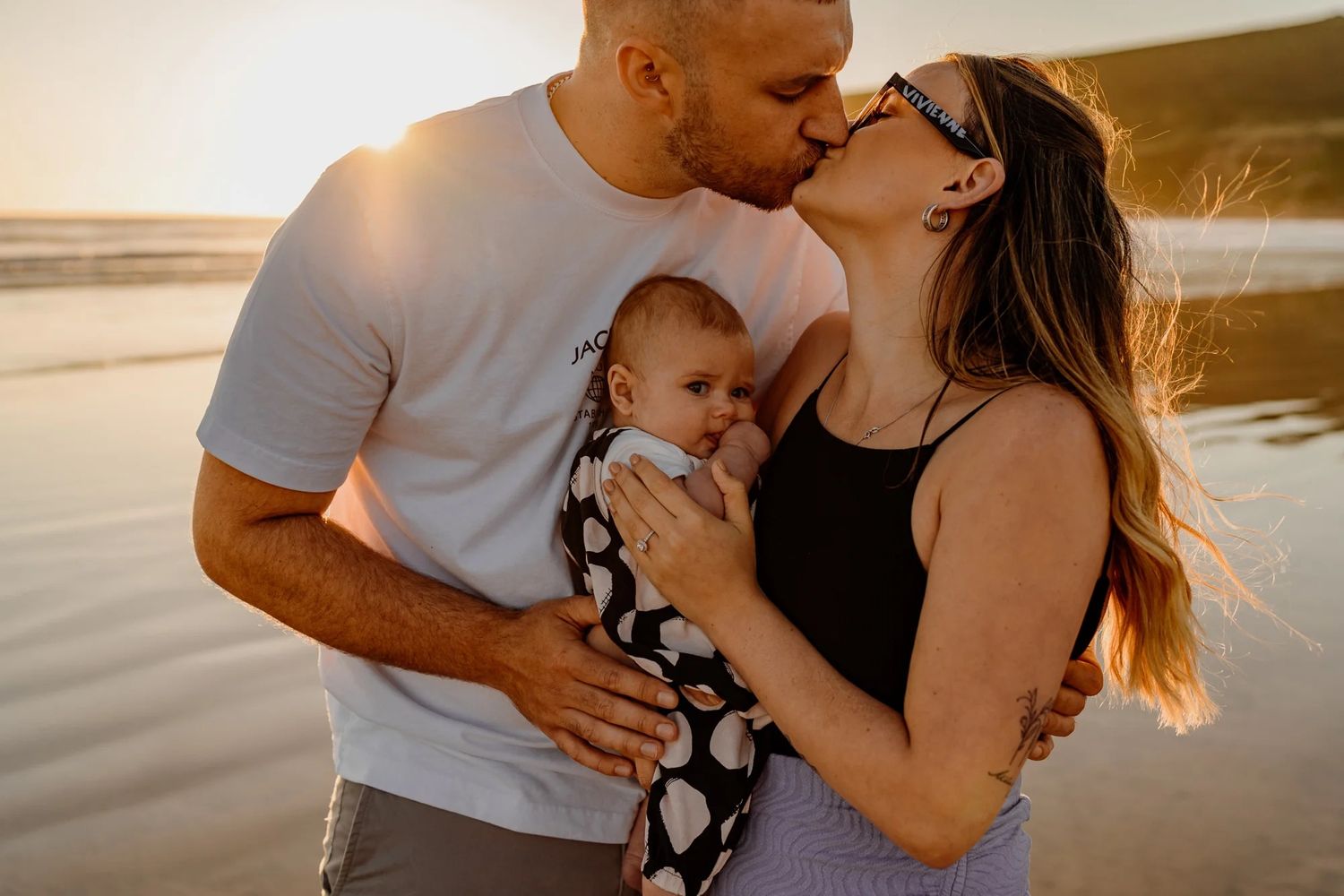A family shares an intimate moment together on the beach at sunset.