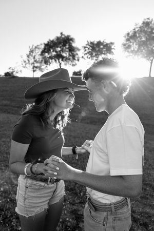 A couple enjoying a tender moment together in a sunlit field, with one person wearing a cowboy hat in black and white.