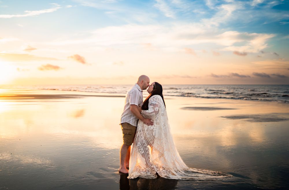 A newlywed couple shares a romantic moment on the beach at sunset with waves crashing on the shore.