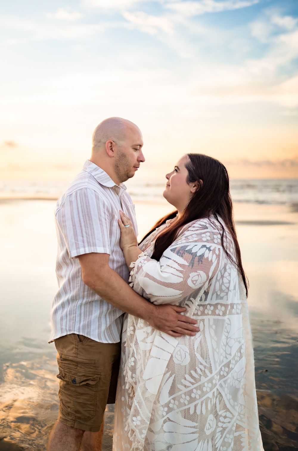 A romantic couple embraces on a sandy beach during a beautiful sunset with glowing warm light.