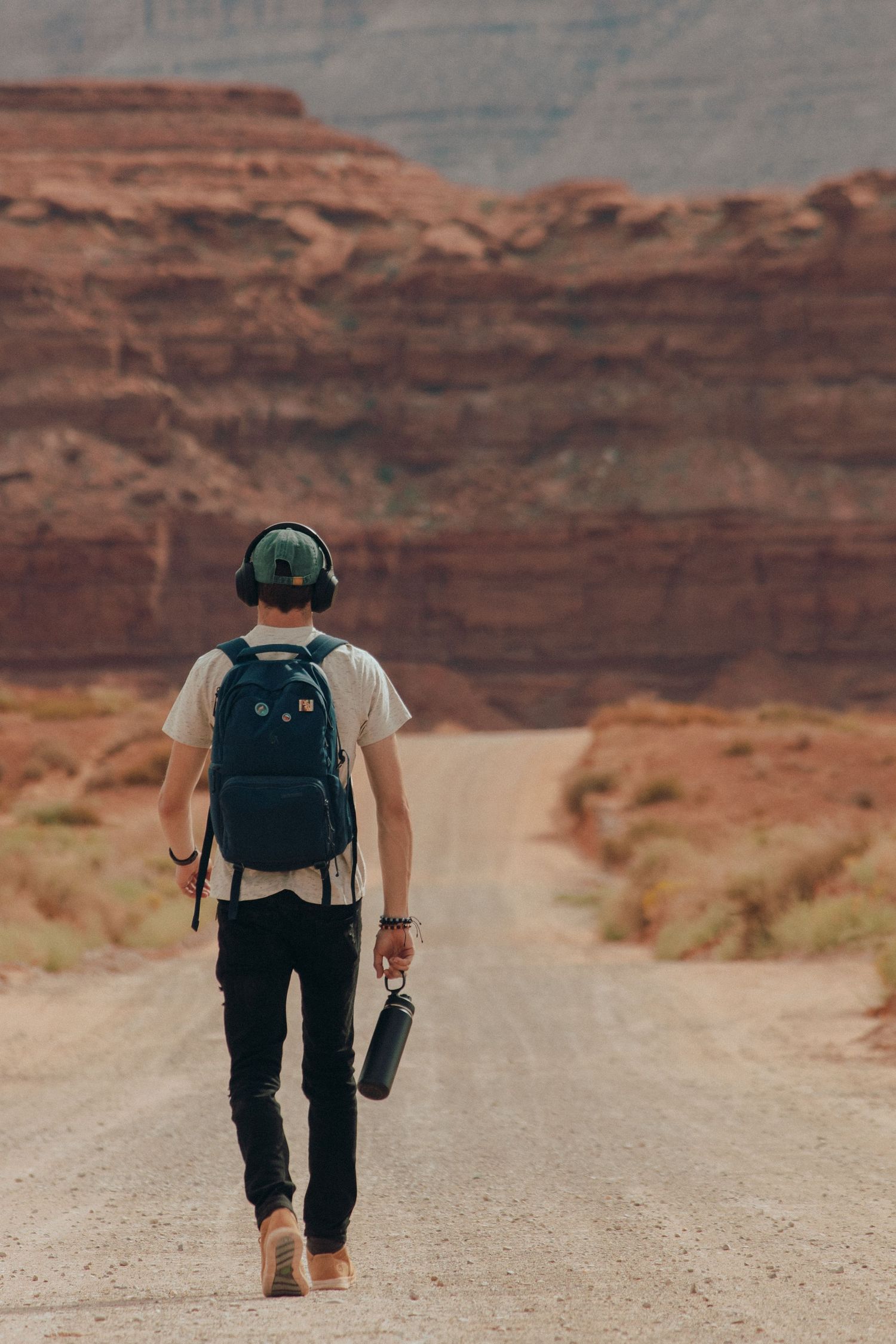Solo traveler walking barefoot on desert road with camera in hand, Utah red rock cliffs. Adventure lifestyle photography by MannyPortraits.