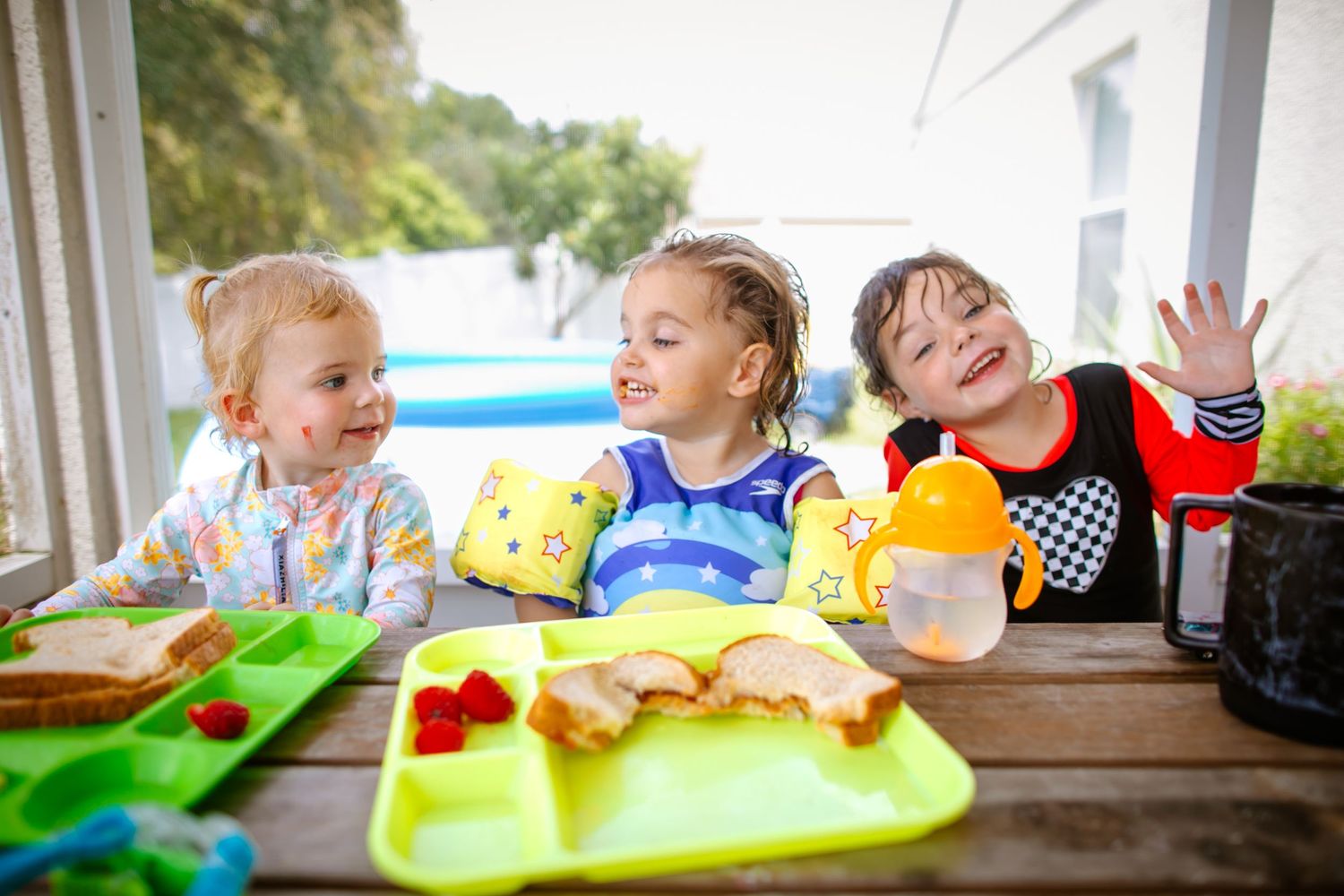 Several children laugh and smile while seated at a long table during lunchtime gathering.