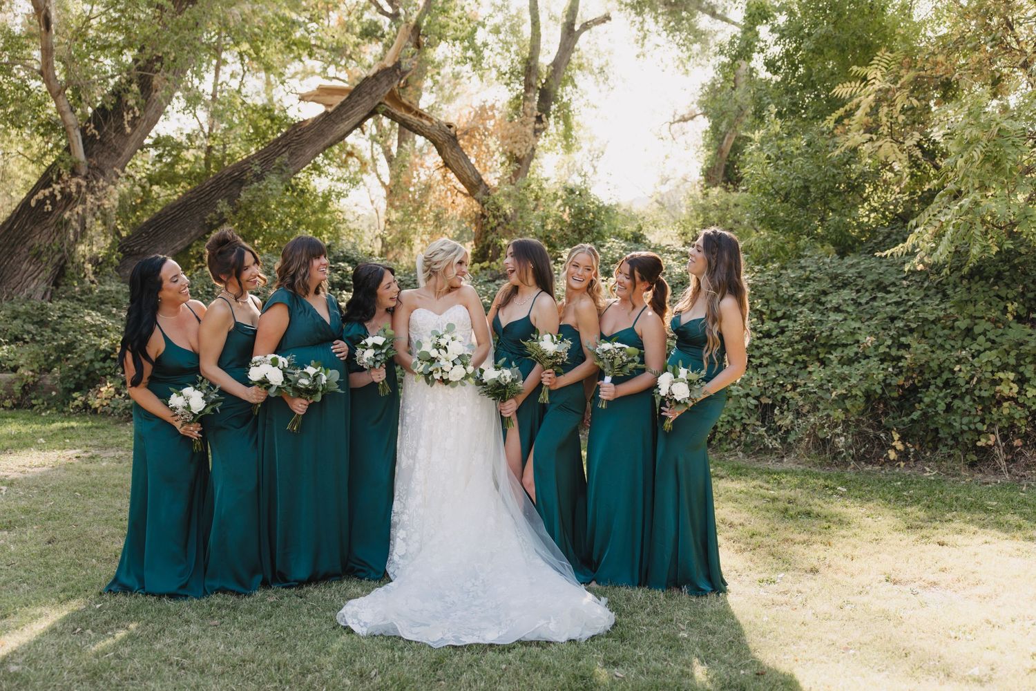 Wedding party in matching teal bridesmaid dresses stand together in a garden setting during outdoor ceremony.