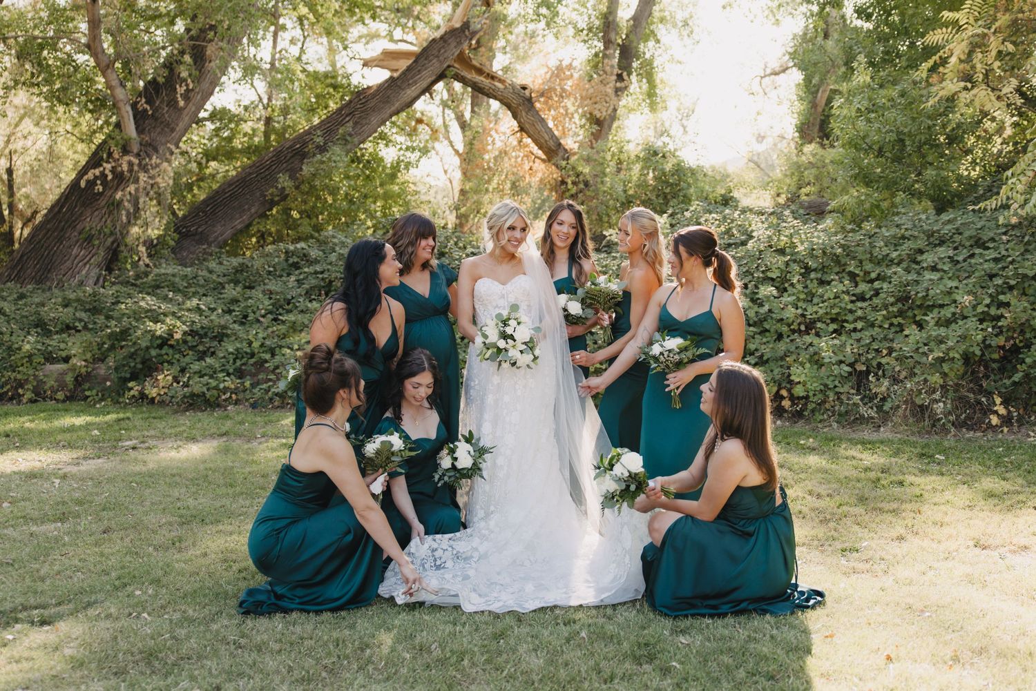 Wedding party in teal bridesmaid dresses poses together outdoors in a natural garden setting during late summer.
