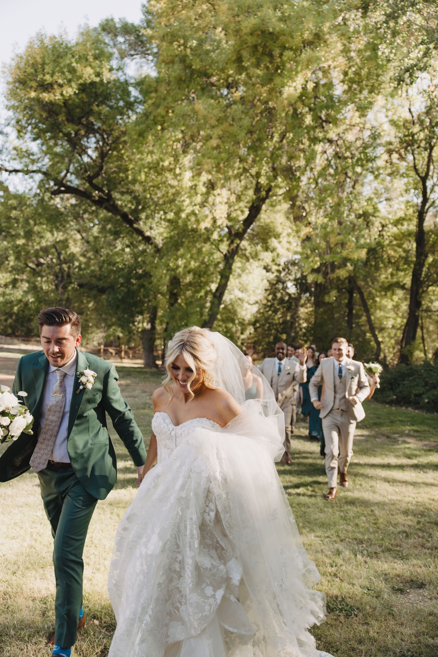 Wedding party walking and laughing together through a sunlit wooded area on a beautiful autumn day.