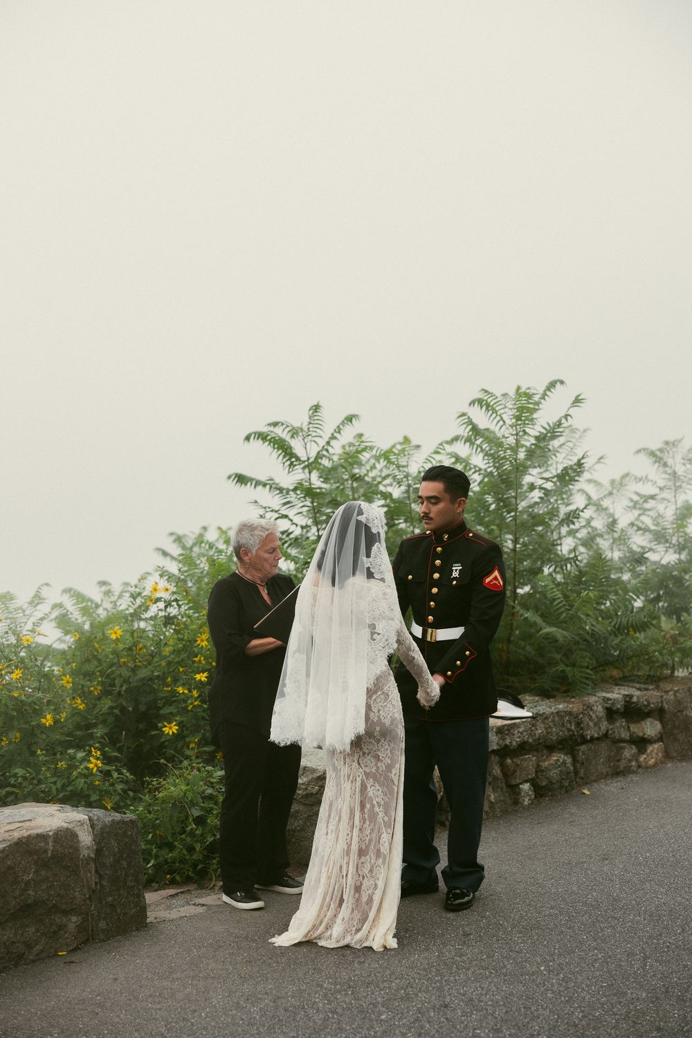 A wedding dress being displayed outdoors against a backdrop of greenery and stone walls.