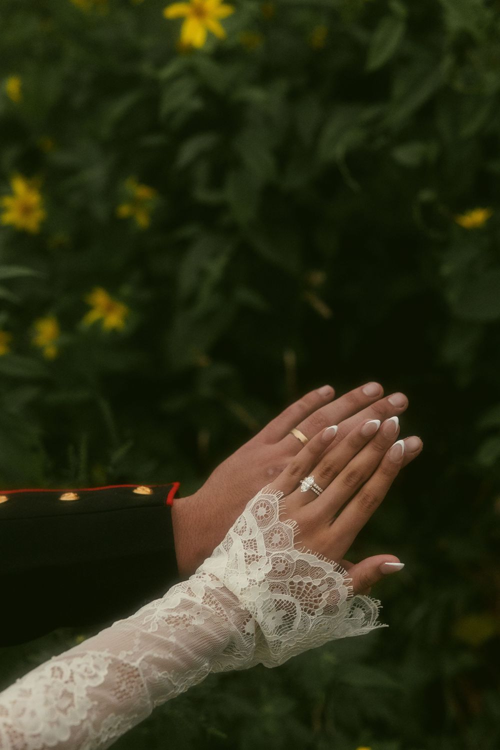 Elegant lace sleeve and wedding ring detail against a dark green garden background.