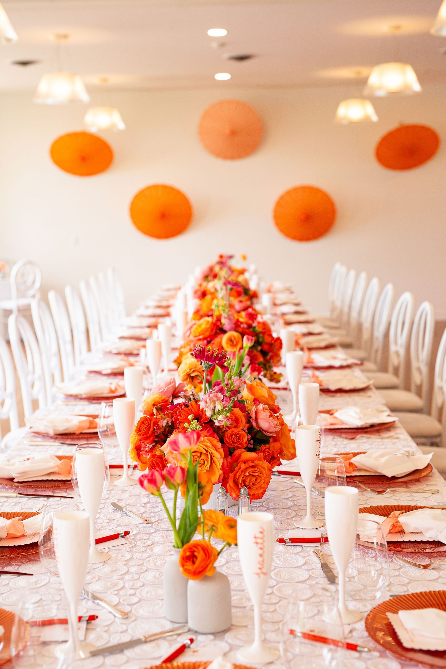 Elegant wedding reception table setting with bright coral and orange floral centerpieces in a white banquet hall.