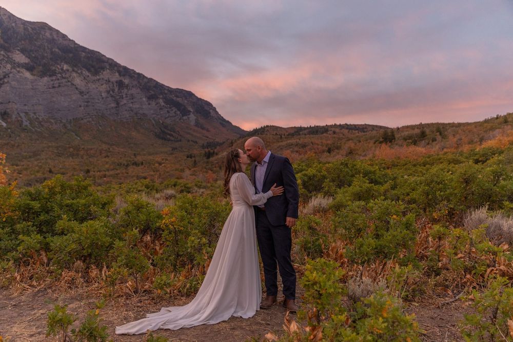 A couple shares an intimate moment at sunset with mountains and autumn foliage creating a romantic backdrop.