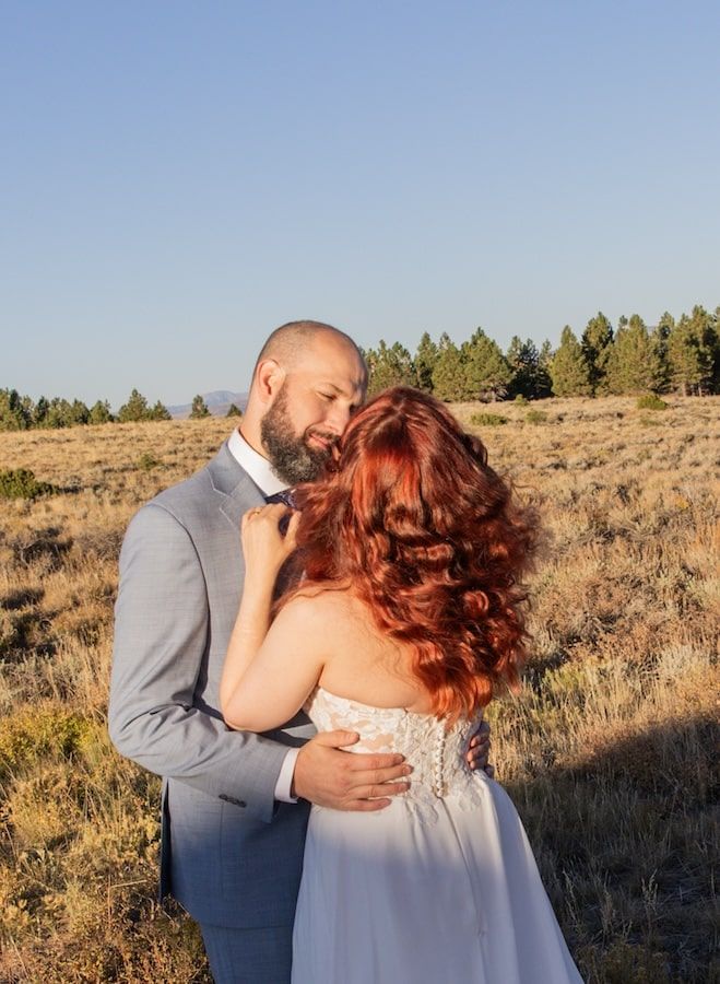 A romantic moment shared between a couple in a gray suit and blue dress at sunset in a desert landscape.