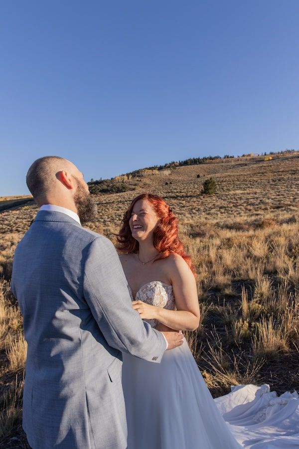 A couple shares intimate moments in their wedding attire against a desert mountain landscape at sunset.